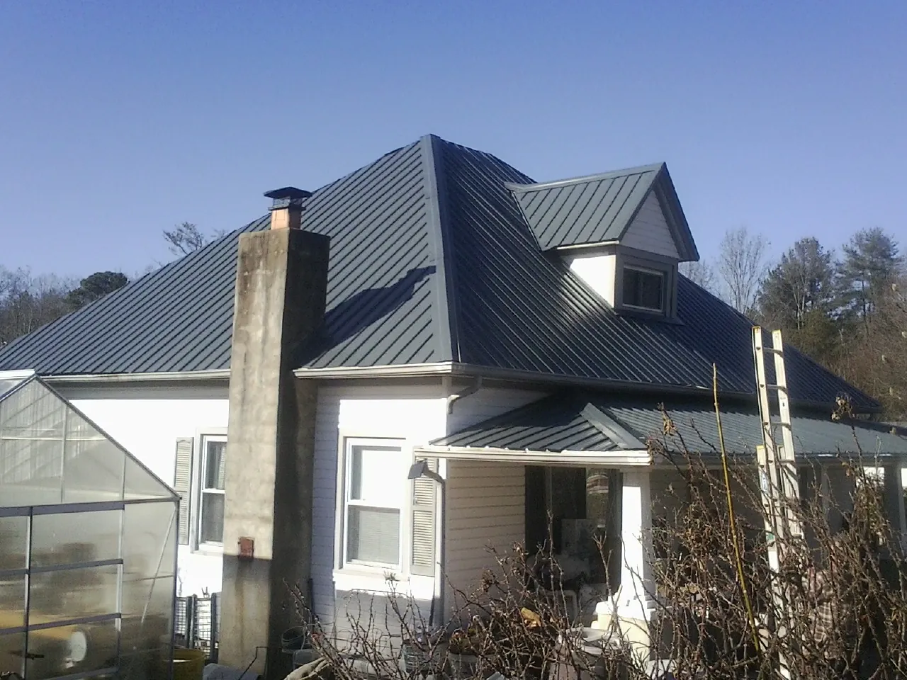 Dark blue standing seam metal roof on a white farmhouse with dormer — Slate & Tile Roof Repair by Roofing Brothers in Lake Pleasant
