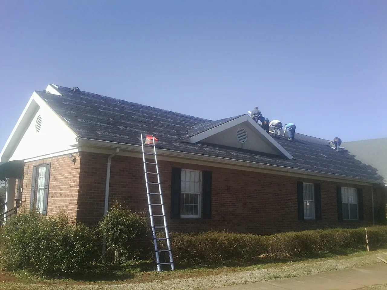 Crew tearing shingles off a brick ranch roof with a ladder set — Emergency Roof Repair work by our crew in Lake Pleasant
