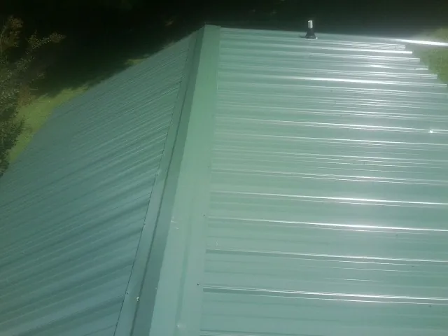 New green metal panels meeting at the ridge of a roof — Flat Roof Repair work by our crew in Lake Pleasant