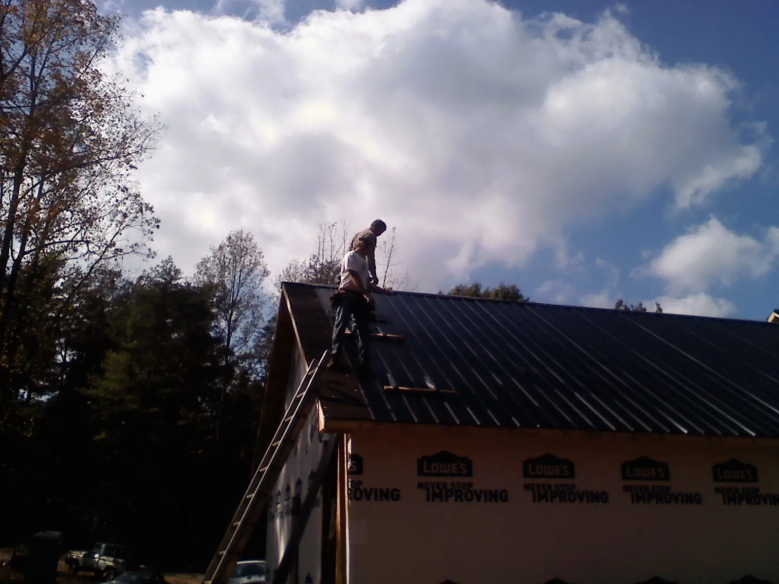 Roofer fastening dark metal panels high against a cloudy sky, from a Roof Inspection job in Lake Pleasant