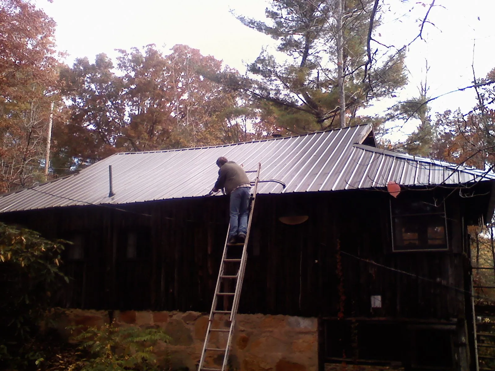 Roofer on a ladder working along the edge of a cabin metal roof in Lake Pleasant