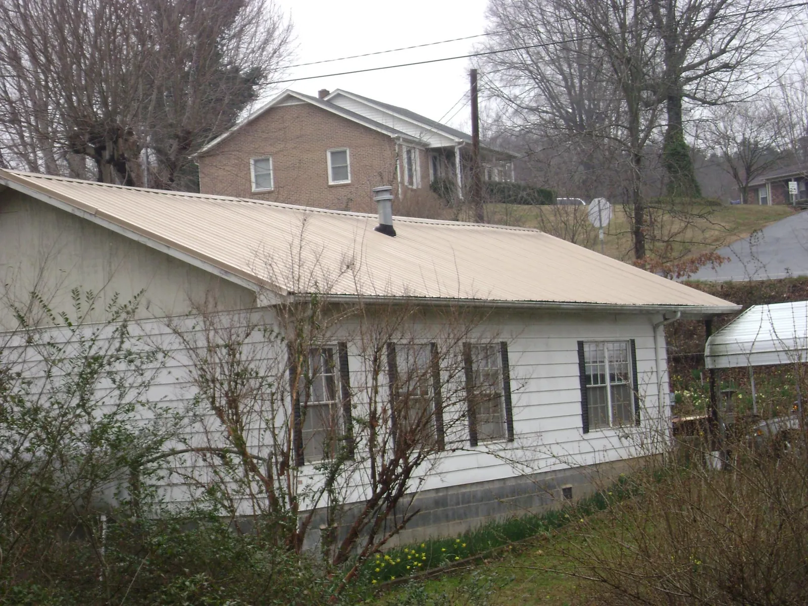 Tan metal roof on a white sided house set into a hillside — Commercial Roofing by Roofing Brothers in Lake Pleasant